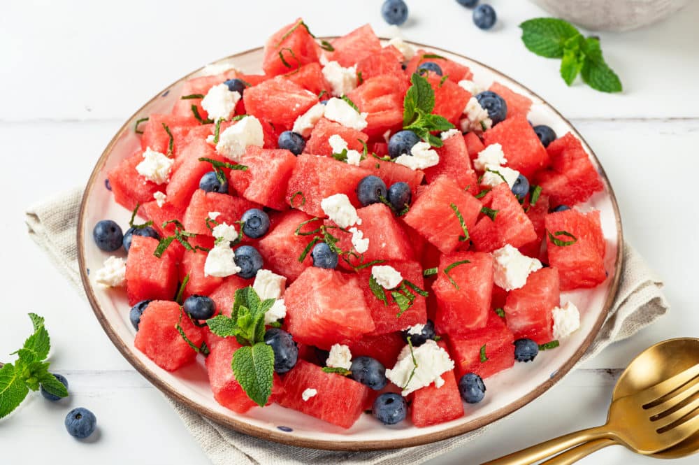 Watermelon feta salad on a white plate topped with fresh mint and a fork and spoon on the side.