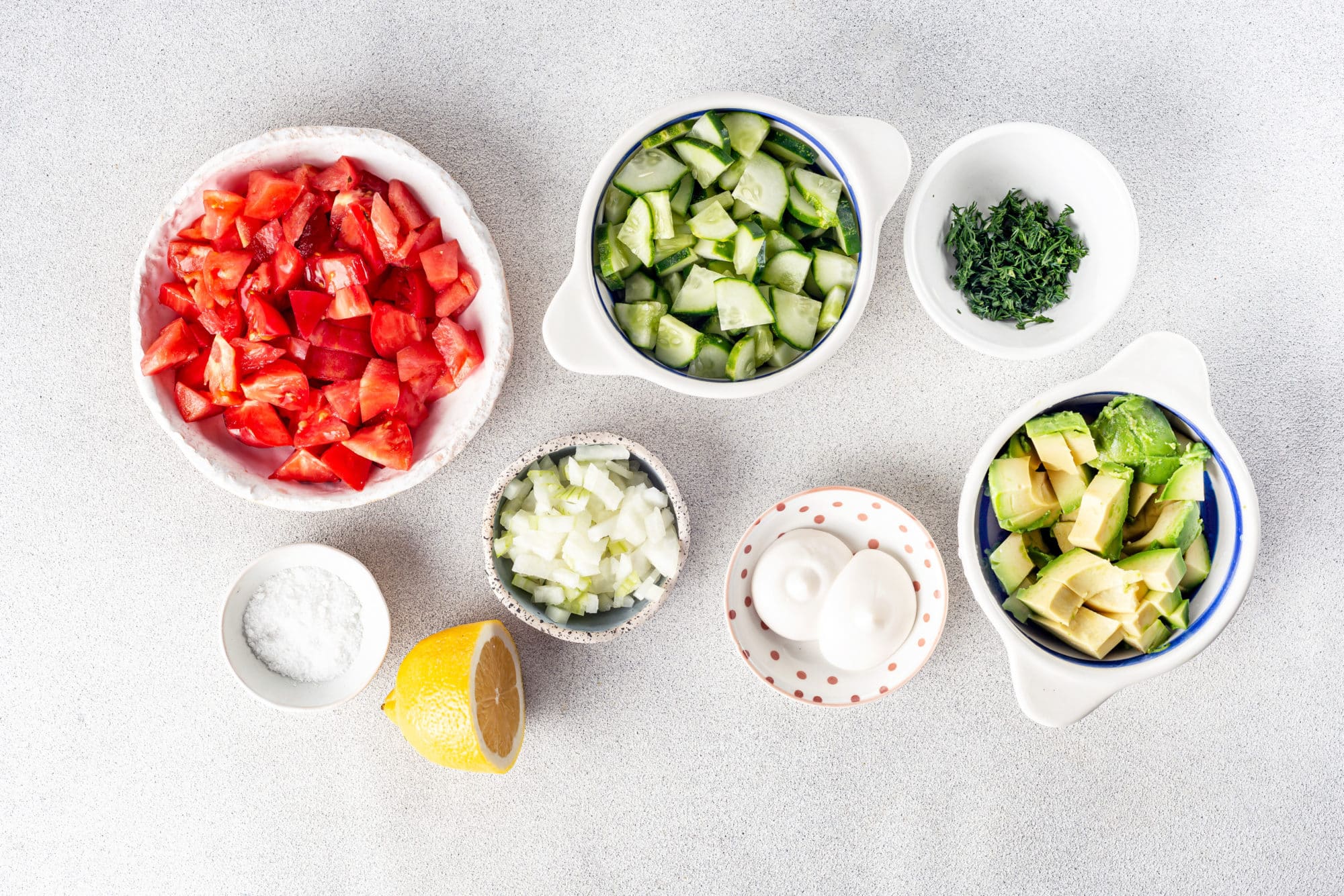 salad ingredients chopped and separated into bowls tomatoes avocado cucumber dill onion mayonnaise a lemon wedge and salt.