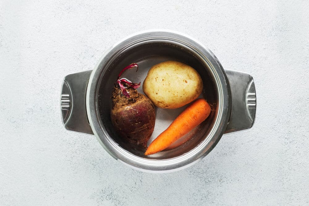 Beet, potato, and carrot boiling in a pot of water.