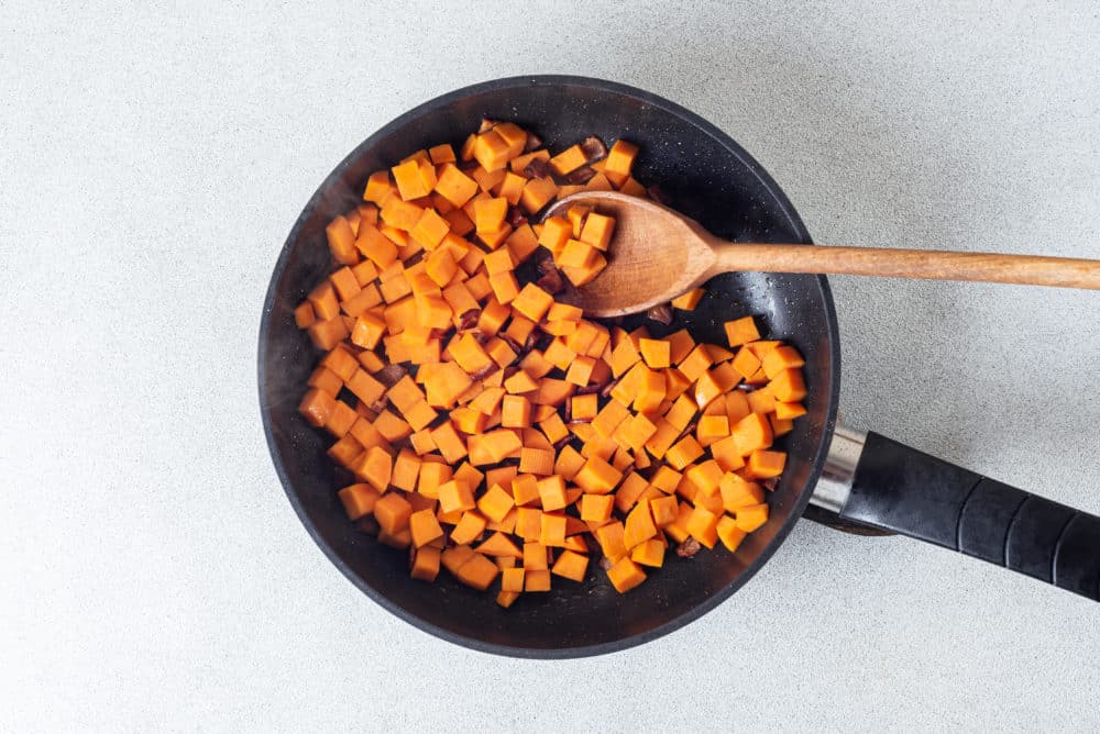 black-skillet-filled-with-sweet-potatoes-and-onion-with-a-wooden-spoon