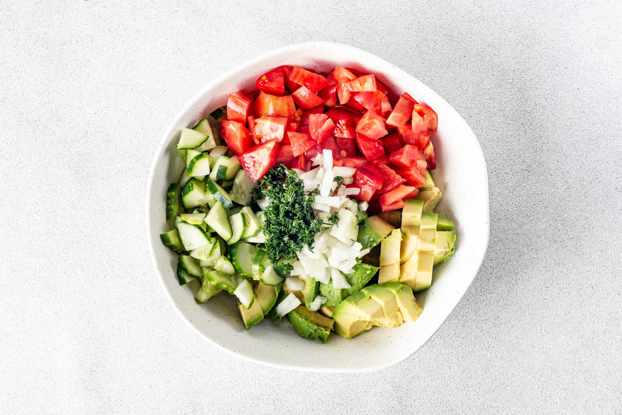 chopped ingredients in a white bowl tomato cucumber onion and dill.