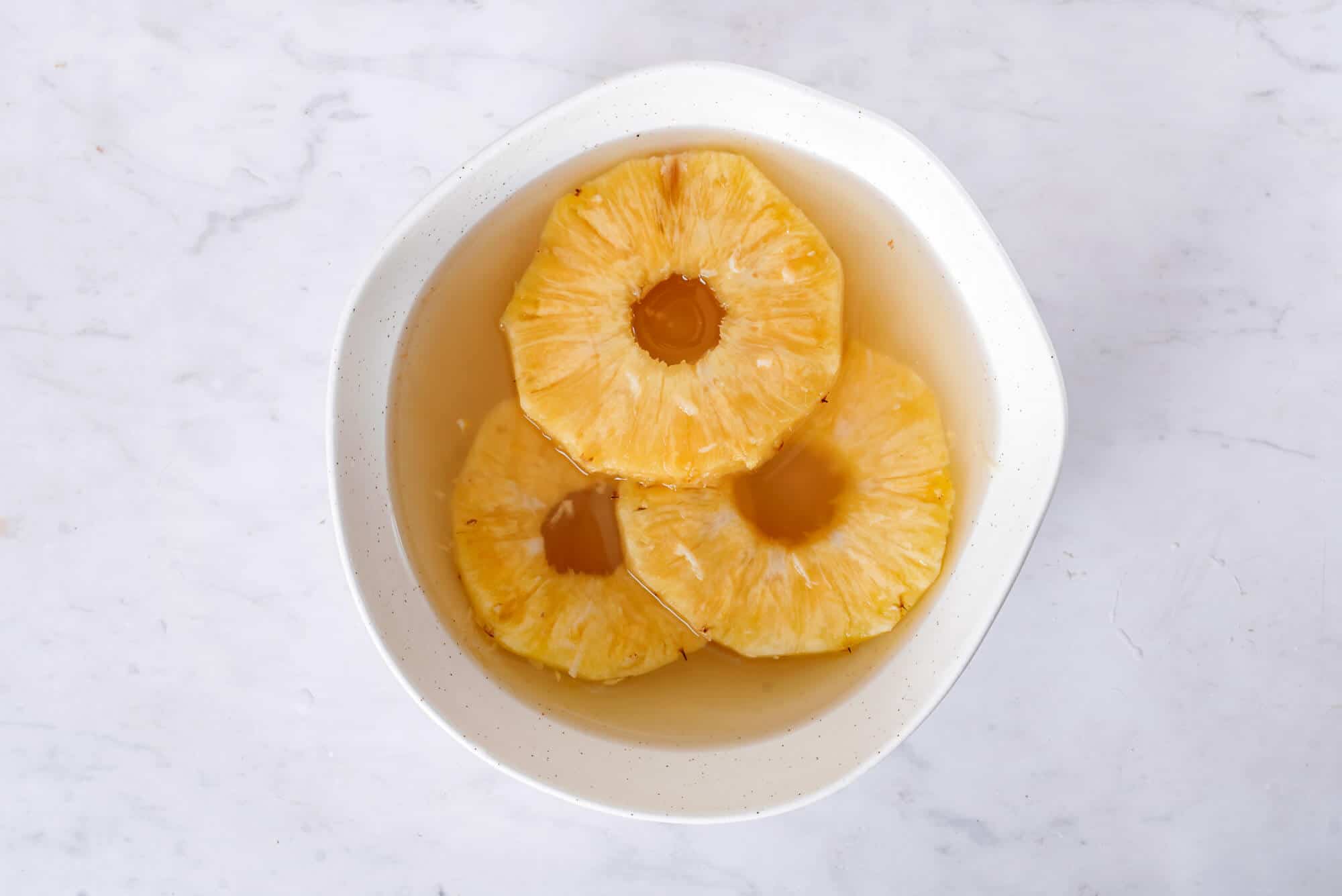 pineapple-slices-marinating-in-a-white-bowl-with-honey-ginger-marinade