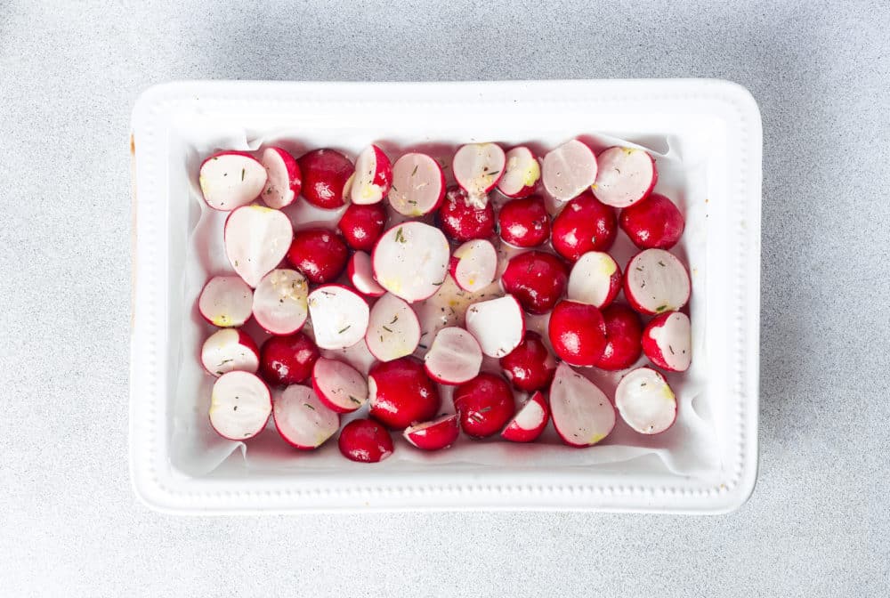 a baking dish filled with seasoned raw radishes.