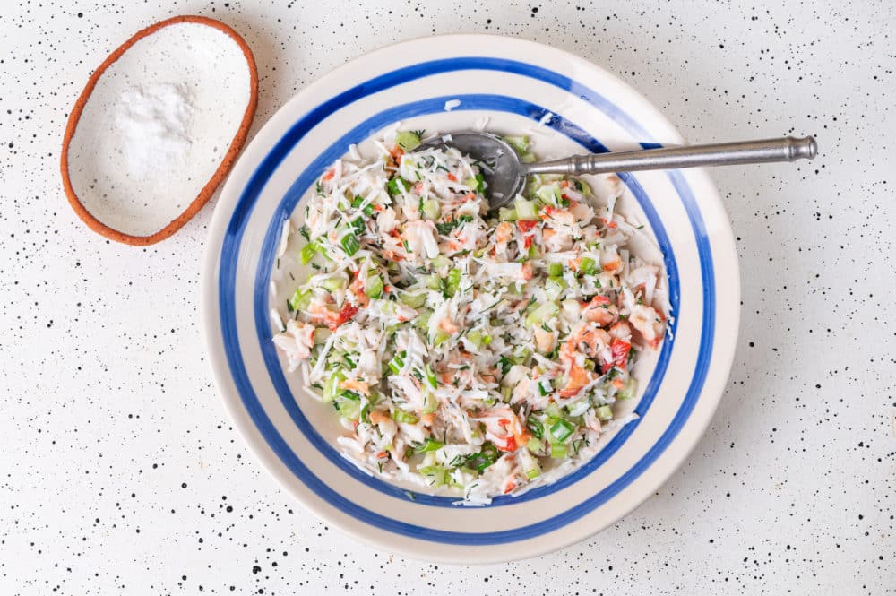 a white bowl with blue stripes with a mixed crab salad and a spoon in it.