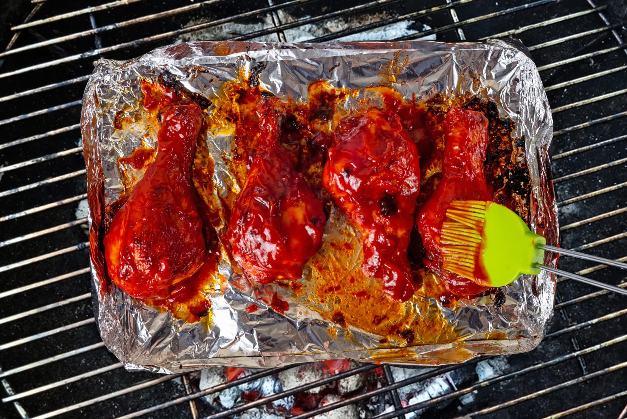 chicken-drumsticks-on-foil-on-a-grill-with-a-baster