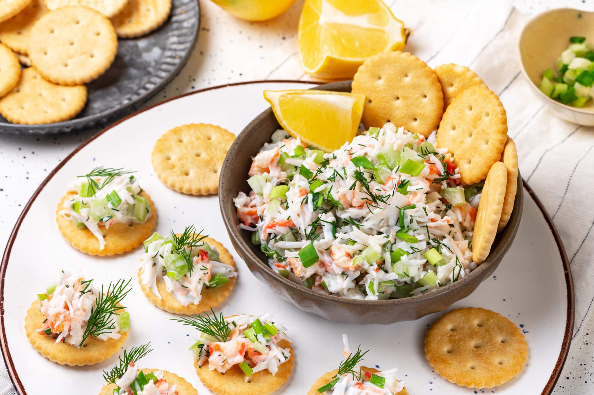 crab salad appetizer in a bowl on a plate with salad on crackers with dill on top.