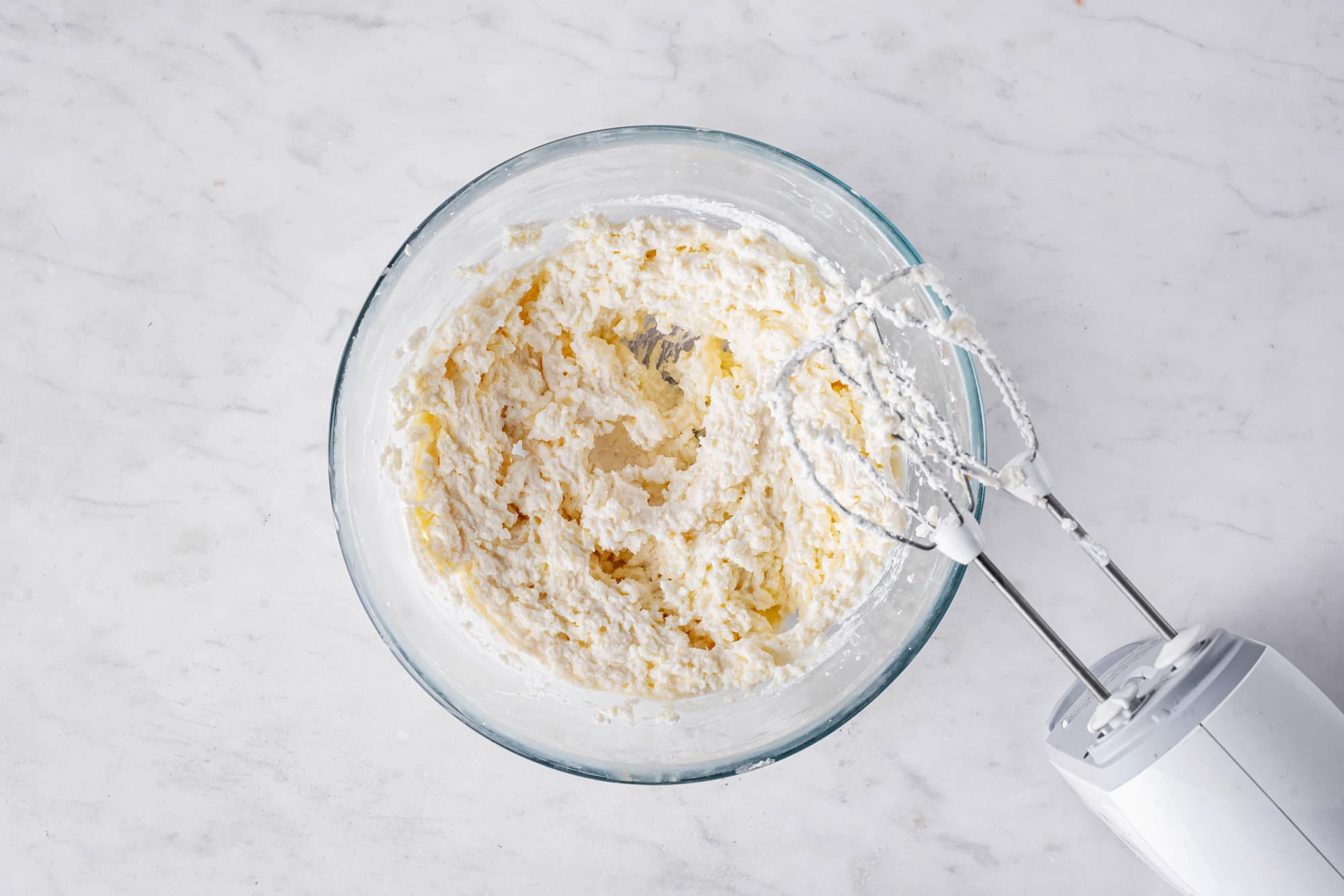 ricotta cream or pumpkin cake roll in a clear bowl with hand mixer.