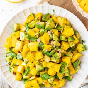 Mango salad with avocado, red onion, dill, and parsley on a white textured plate.