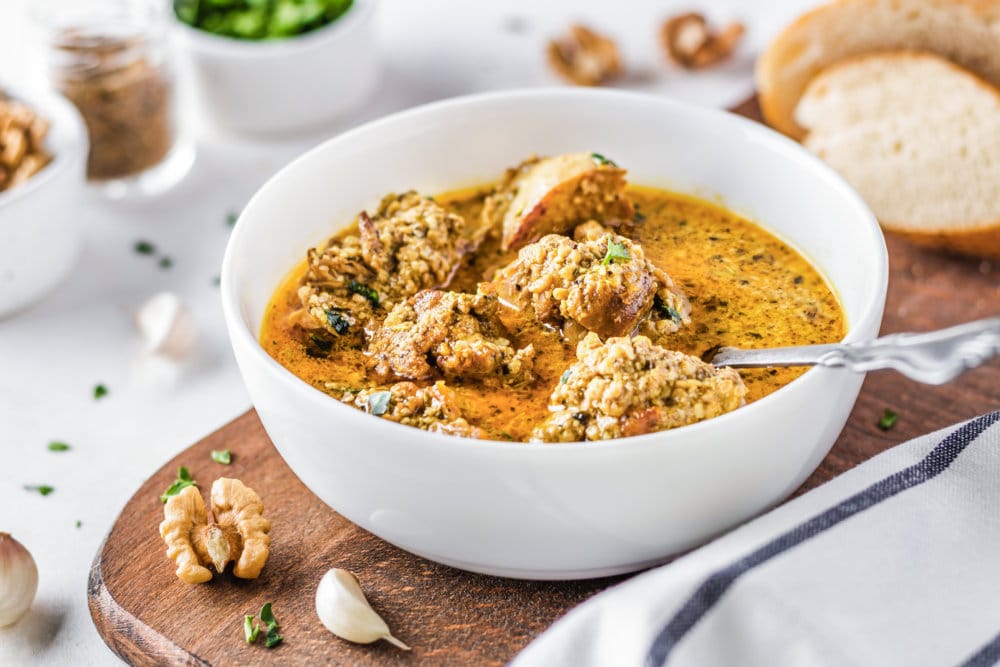 georgian chicken in broth in a white bowl with a spoon on a wooden board.