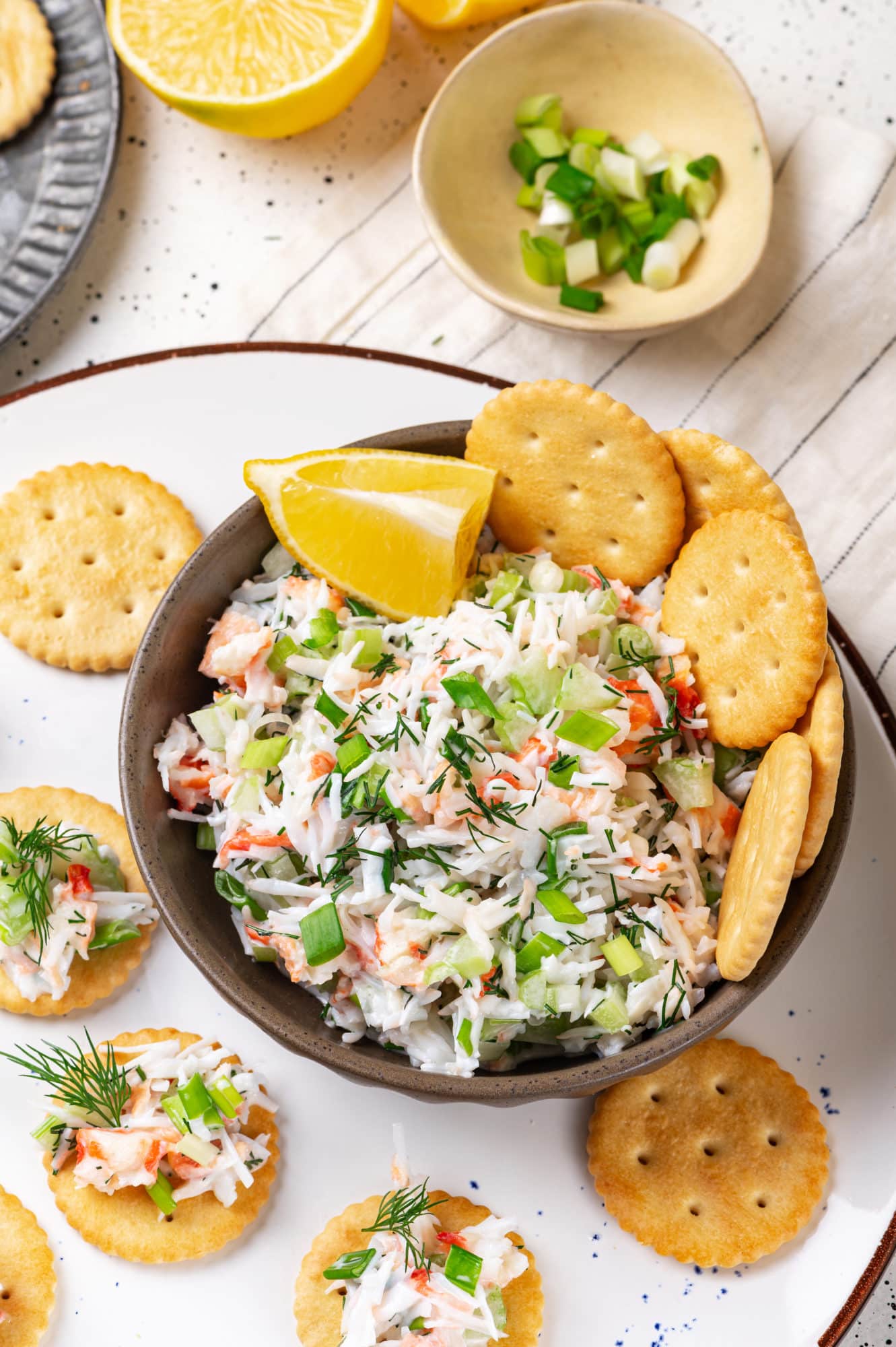 a crab salad in a bowl with crackers in it and a white plate with crackers and salad on them.