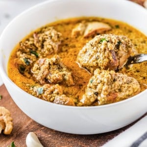 Georgian chicken in a white bowl on a wooden board with a spoon.