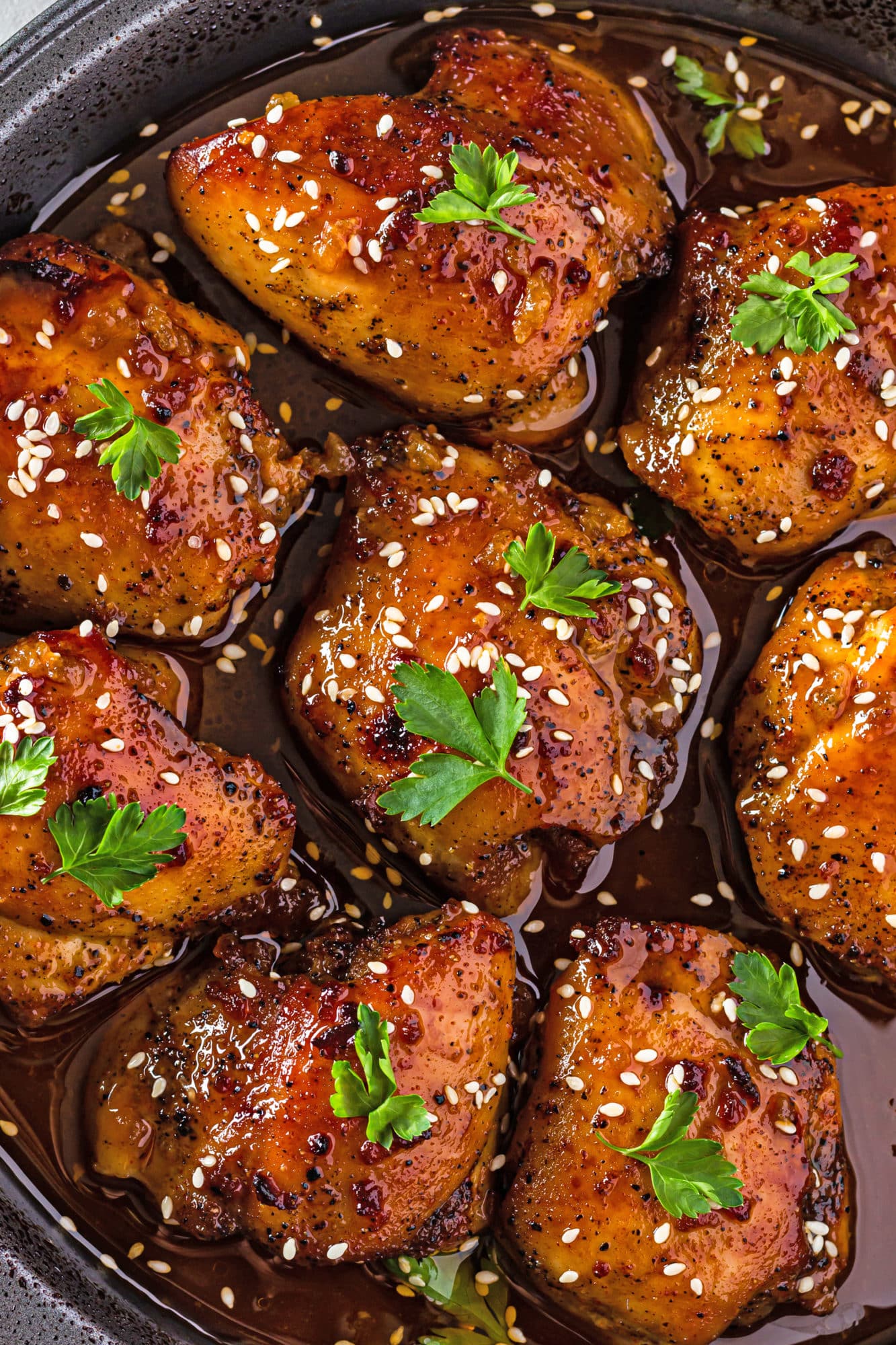 close up of soy sauce chicken thighs cooked in marinade with sesame seeds and parsley on top.