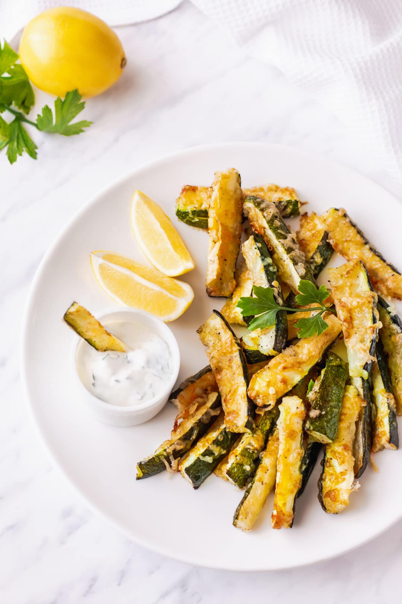 zucchini-bites-on-a-white-plate-with-a-bowl-of-dip-and-lemon-wedges-on-the-side