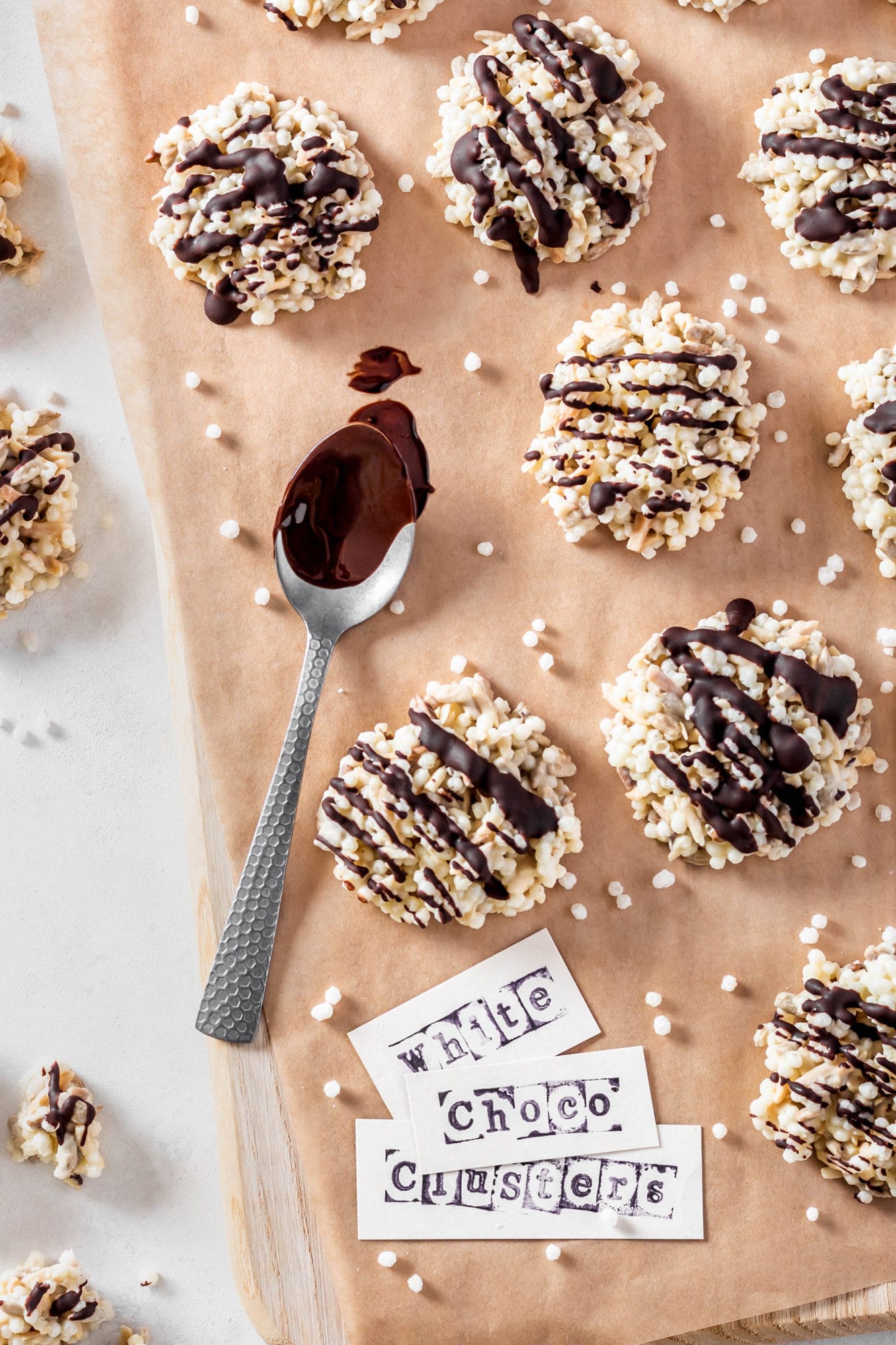 Rice puffs clusters on parchment paper with a spoon of chocolate and white paper labels.