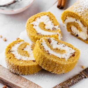 pumpkin-cake-roll-sliced-on-parchment-paper-and-a-wooden-board-with-a-knife