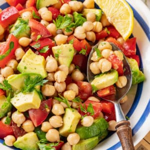 Chickpea avocado salad in a blue striped bowl with parsley sprinkled throughout, and a spoon on the side.