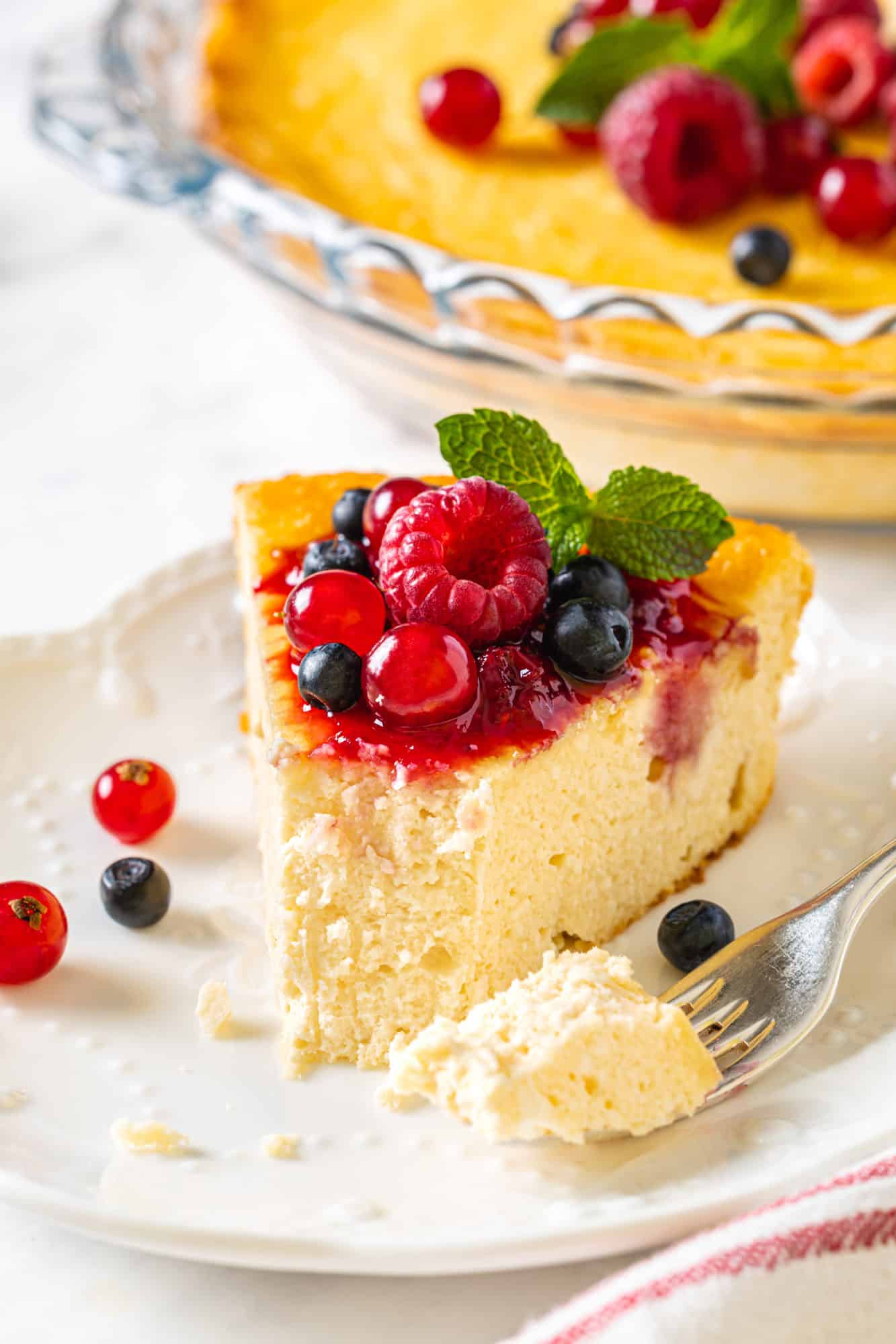 slice of farmer's cheese sweet casserole with fresh berry jam on top on a white plate and silver fork.