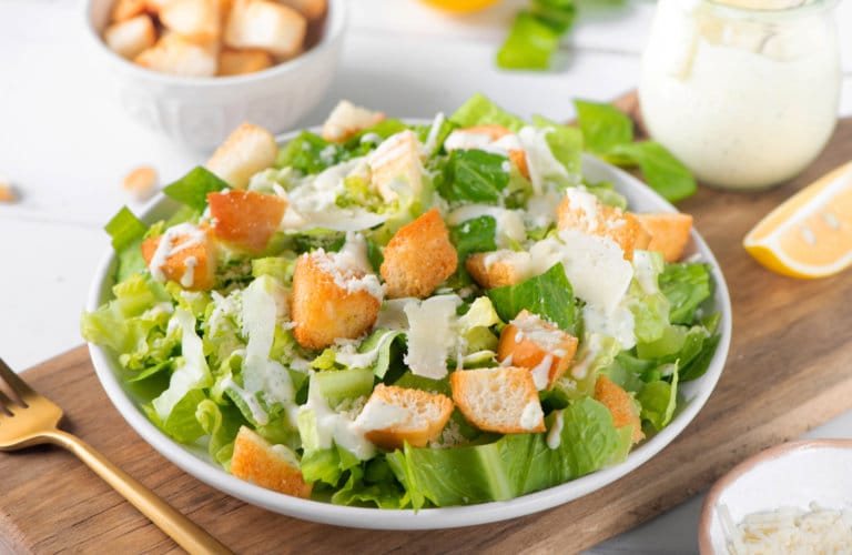 Caesar salad on a white plate with croutons and drizzled dressing on top.
