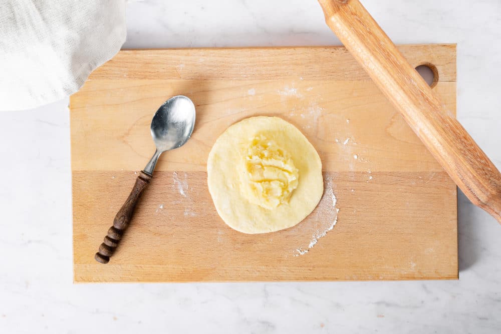 dough-on-a-wooden-board-with-potato-filling-with-a-rolling-pin-and-a-spoon
