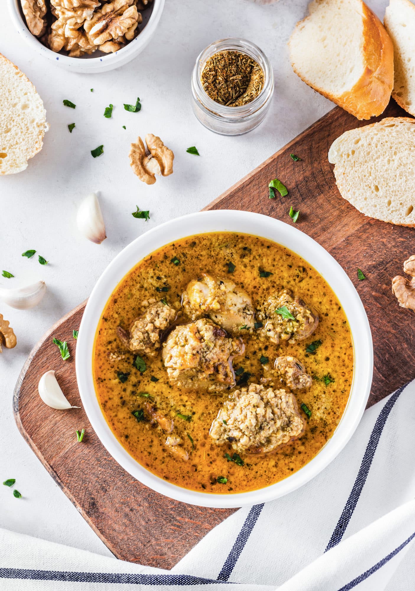 Georgian chicken in a white bowl on a wooden board with sliced bread.