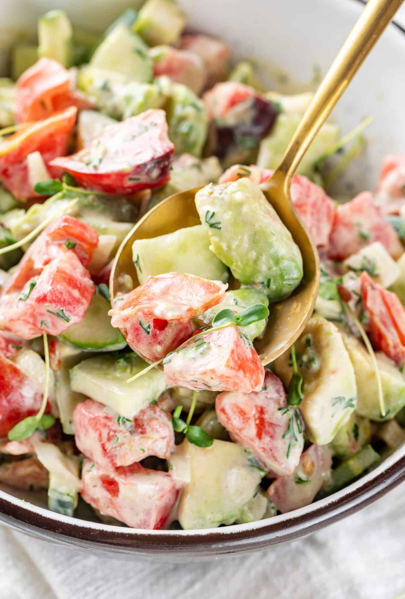 close up of avocado tomato cucumber salad on a gold spoon and in a bowl.