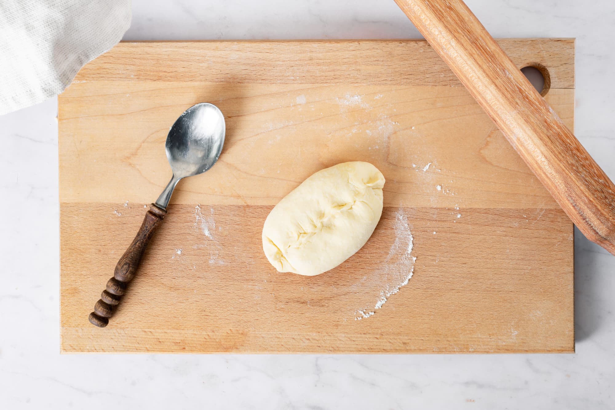 A piroshok on a wooden cutting board with a spoon and a wooden rolling pin on the side.