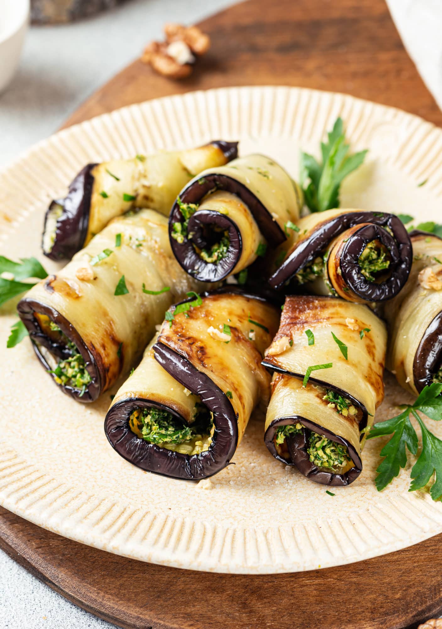 a beige plate with herb filled eggplant rolls with parsley.