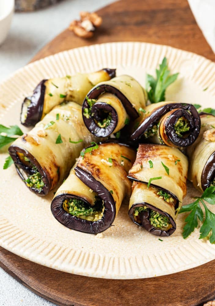 eggplant rolls filled with herbs on a white plate with parsley.