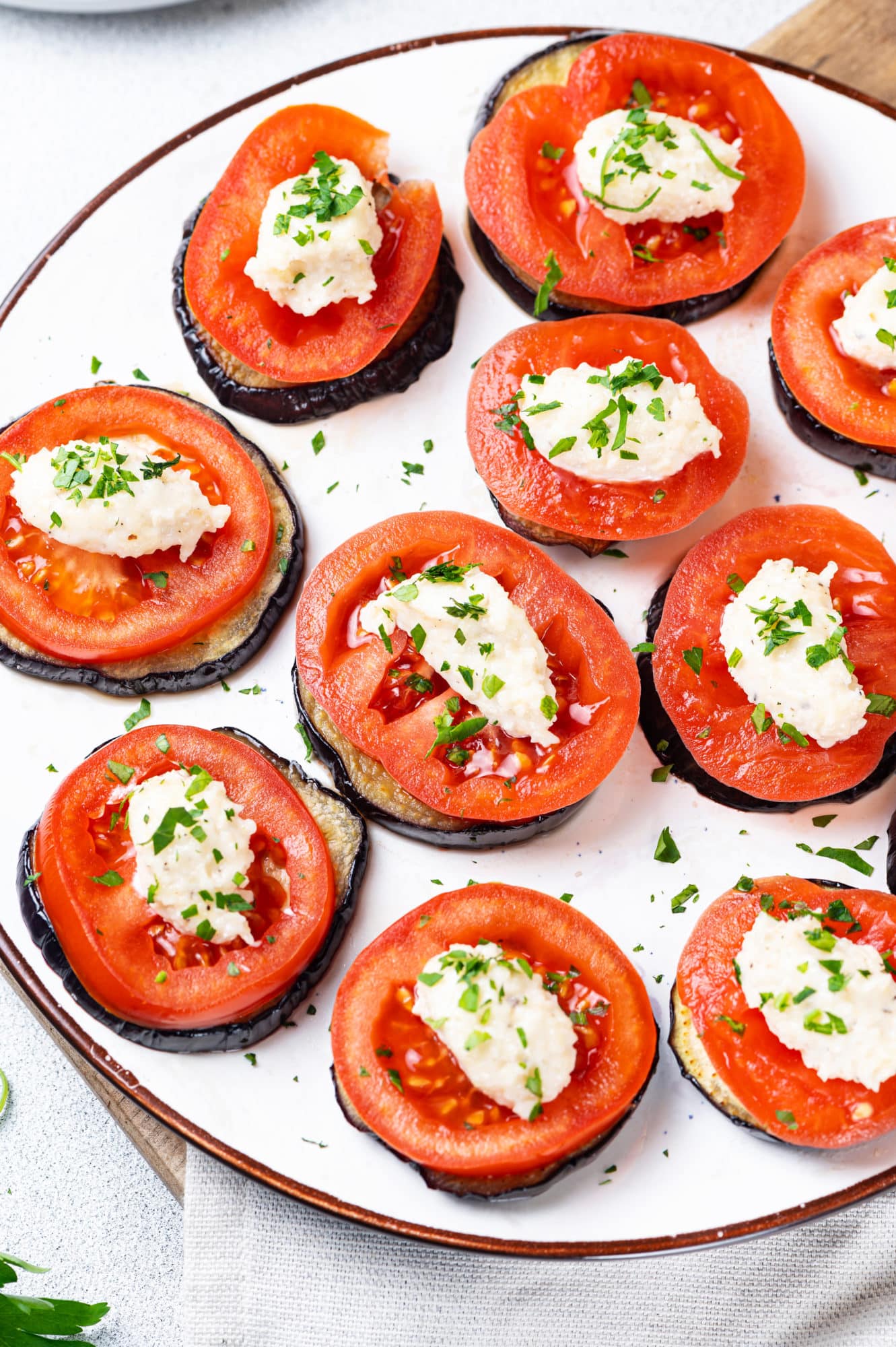 eggplant slices under tomato slices with a creamy topping on a white plate making up small individual appetizers.