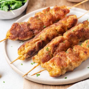 white-plate-with-four-chicken-skewers-on-a-brown-board-lemon-wedge