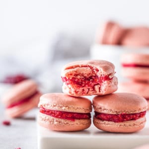 Stacked raspberry macarons on a white board with a bite taken out.