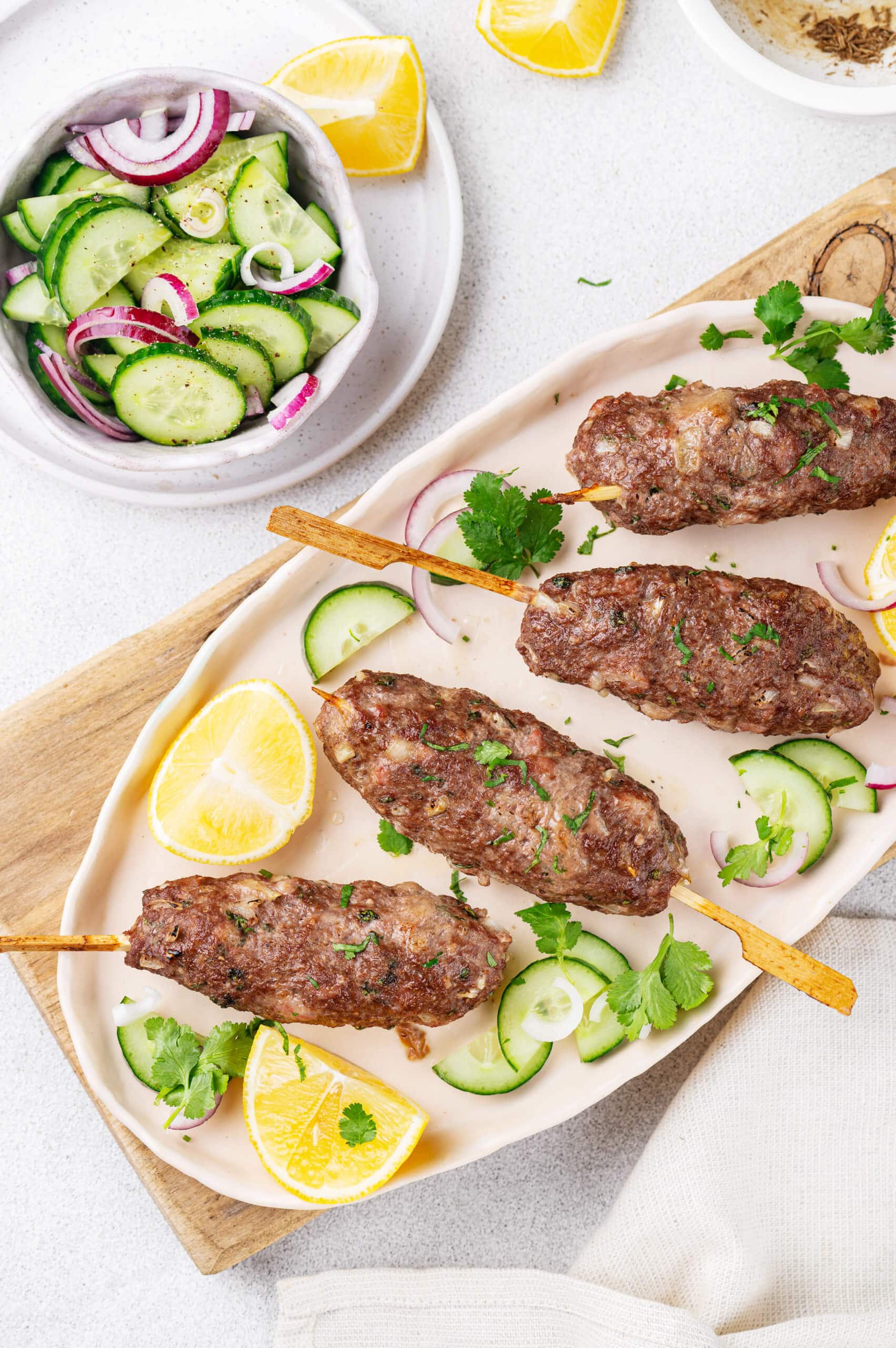 lamb kofta kebabs on a white oblong plate on top of a wooden serving board 