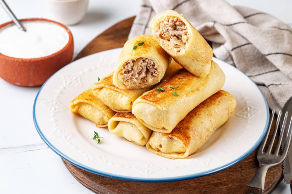 crepes filled with chicken stacked on a white plate with a blue rim.