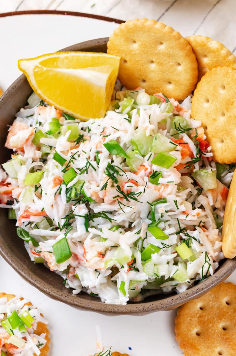 crab salad snack in a bowl with a lemon wedge and crackers.