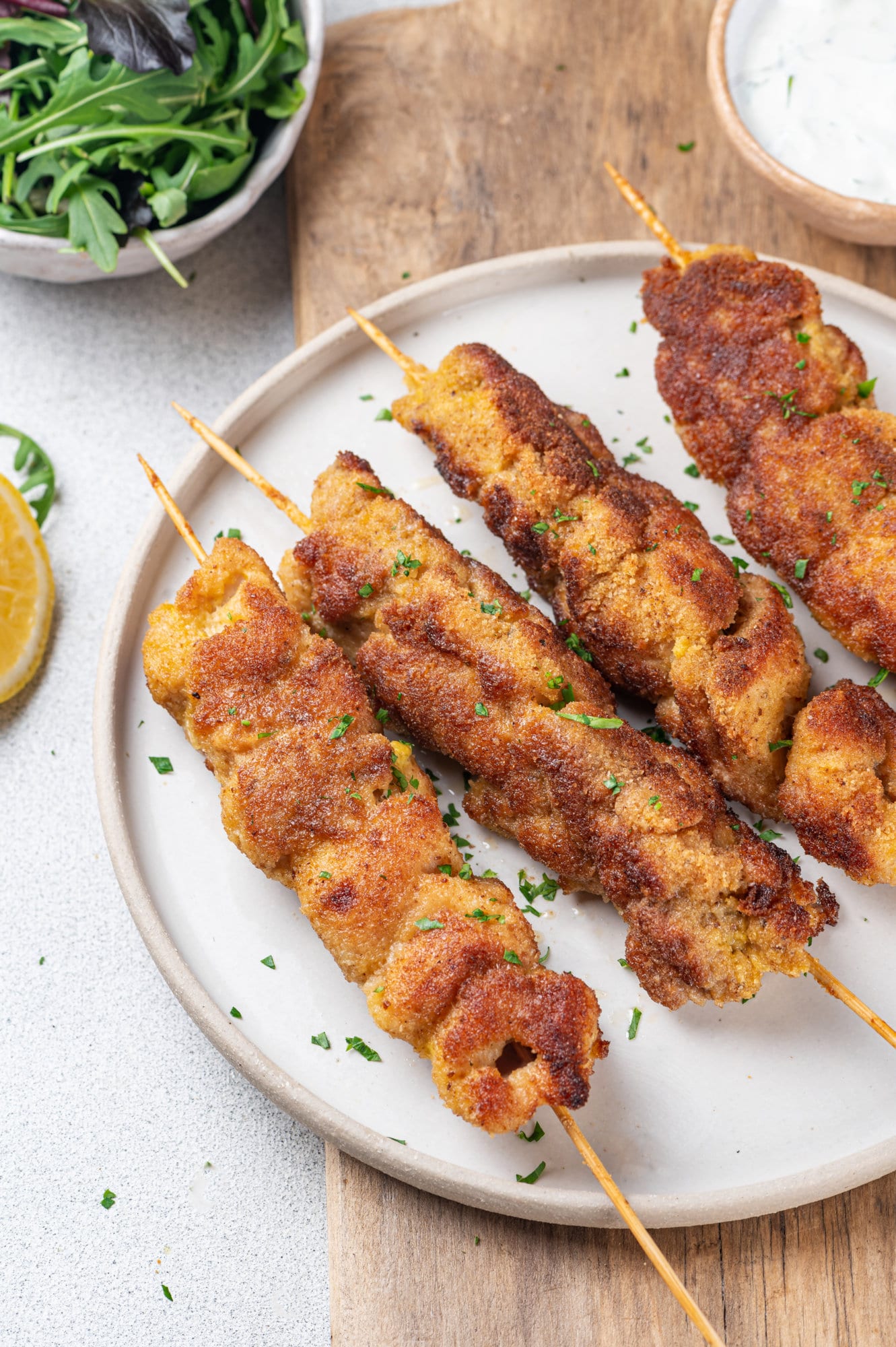 Tender Breaded Chicken in the Oven on Skewers white-plate-with-four-chicken-skewers-on-a-brown-board