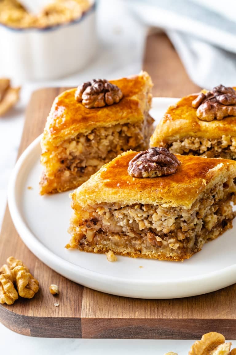 baklava-pieces-on-a-white-plate-on-a-wooden-board-with-walnut-pieces-on-top