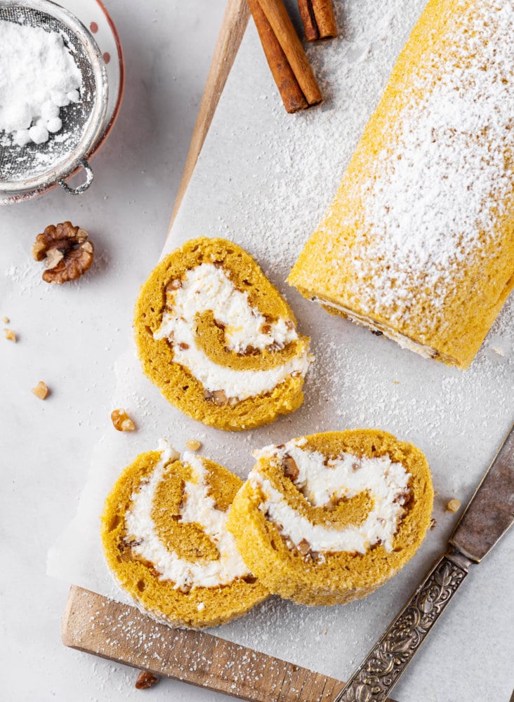pumpkin-cake-roll-sliced-on-parchment-paper-and-a-wooden-board-with-a-knife