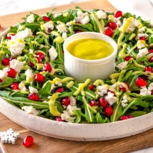 a white plate with a green salad and drizzled green dressing on top and dressing in a small white dish in the center with pomegranate seeds and feta cheese sprinkled on top of the salad.