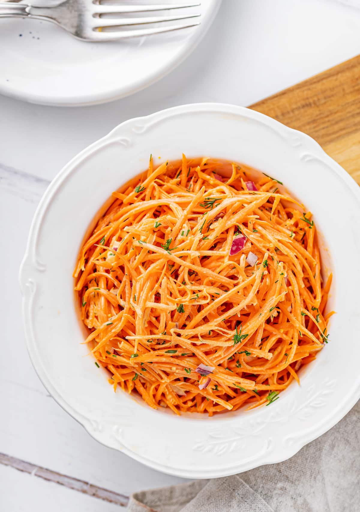 creamy carrot salad in a white shallow plate with dill and red onion mixed with mayonnaise.