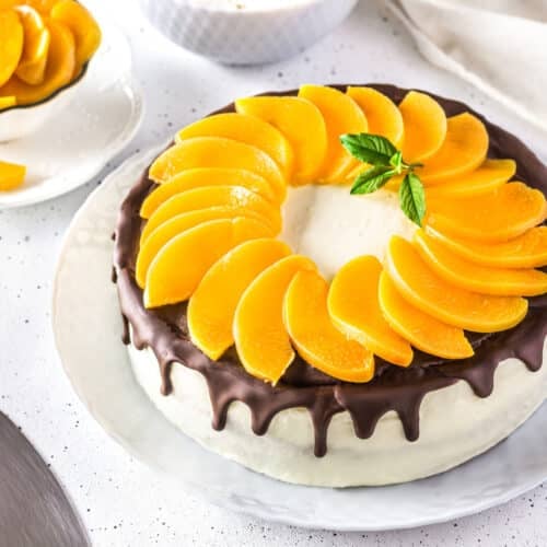 Decorated peach mousse cake with peach slices on a white plate.