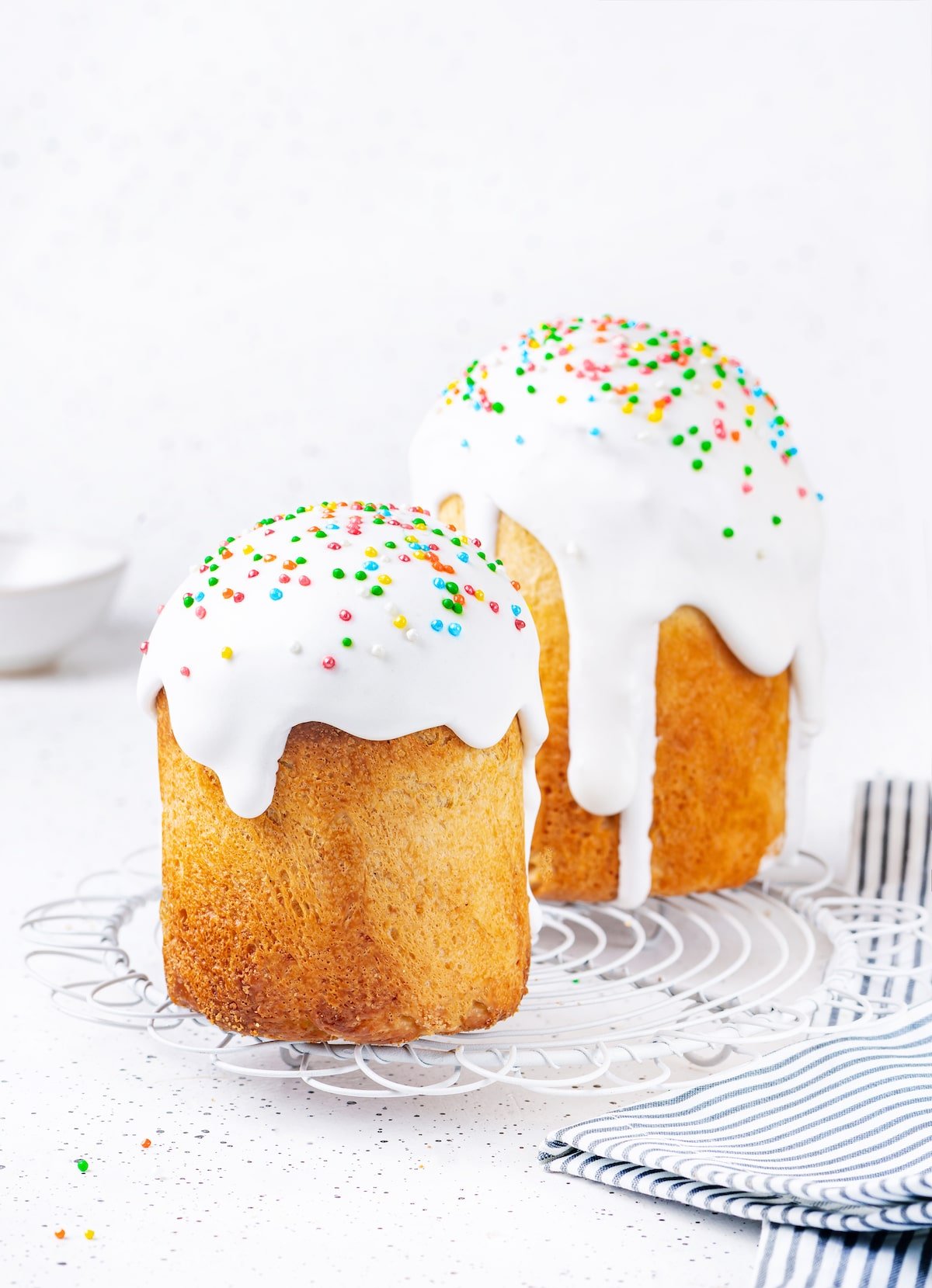 Easter bread soft bread with white icing dripping and topped with colorful sprinkles on white surface. 