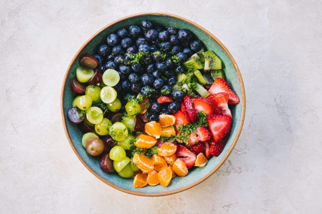 Fruit salad ingredients in a bowl with dressing drizzled on top. 