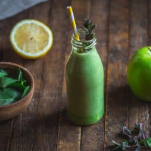 green-smoothie-in-a-glass-with-a-straw-and-mint-with-ingredients-around