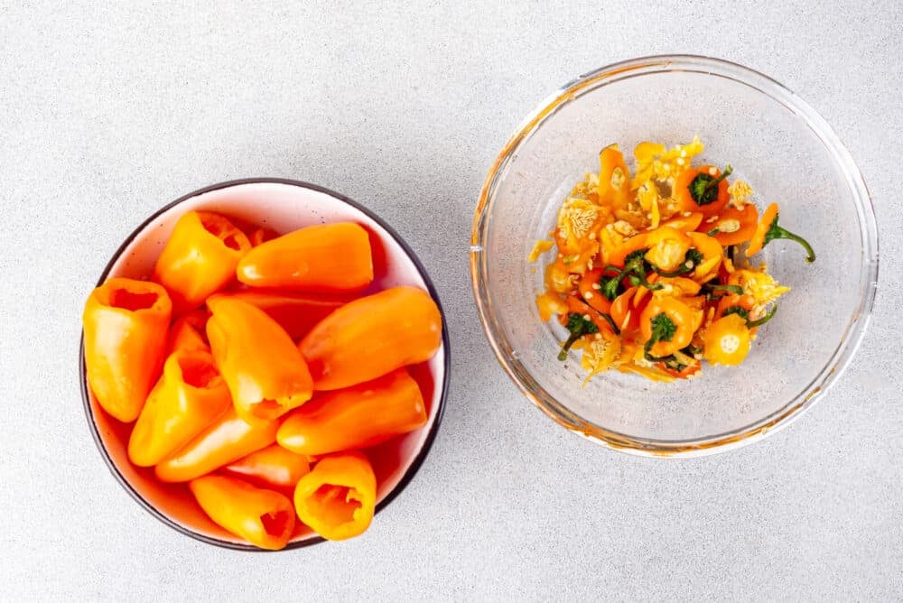 Mini peppers in a bowl with insides cleaned out in a separate bowl.