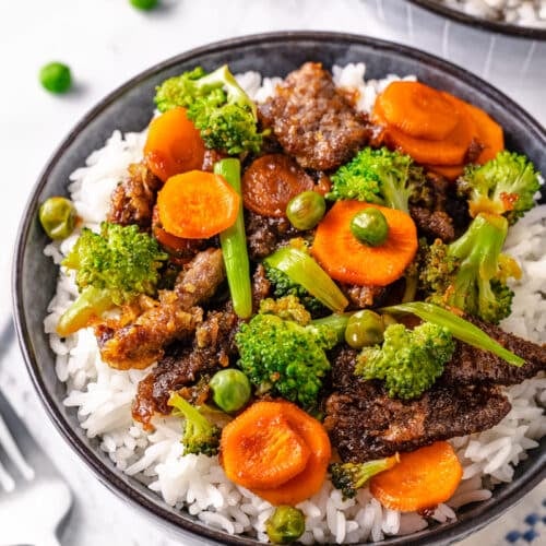 cooked beef with mixed vegetables on white rice in a bowl.