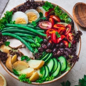 nicoise-salad-in-a-bowl-with-a-wooden-spoon-on-the-side-and-lemon-wedges