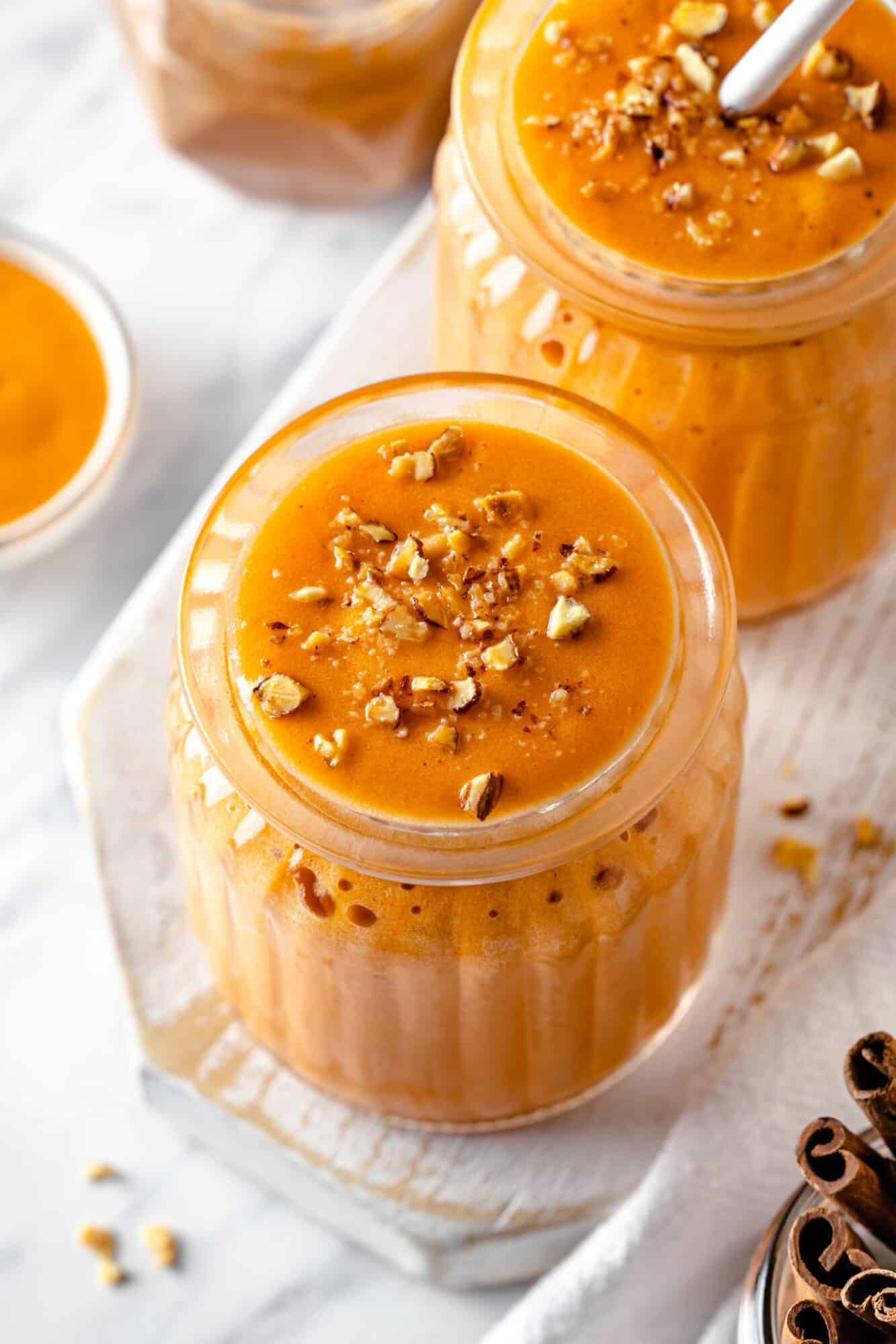 two glasses filled with pumpkin pie smoothie with chopped almonds.