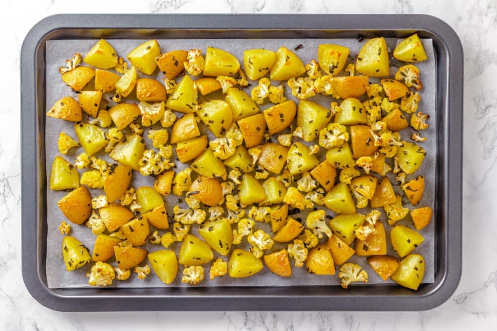 roasted potatoes and cauliflower florets on oven pan.