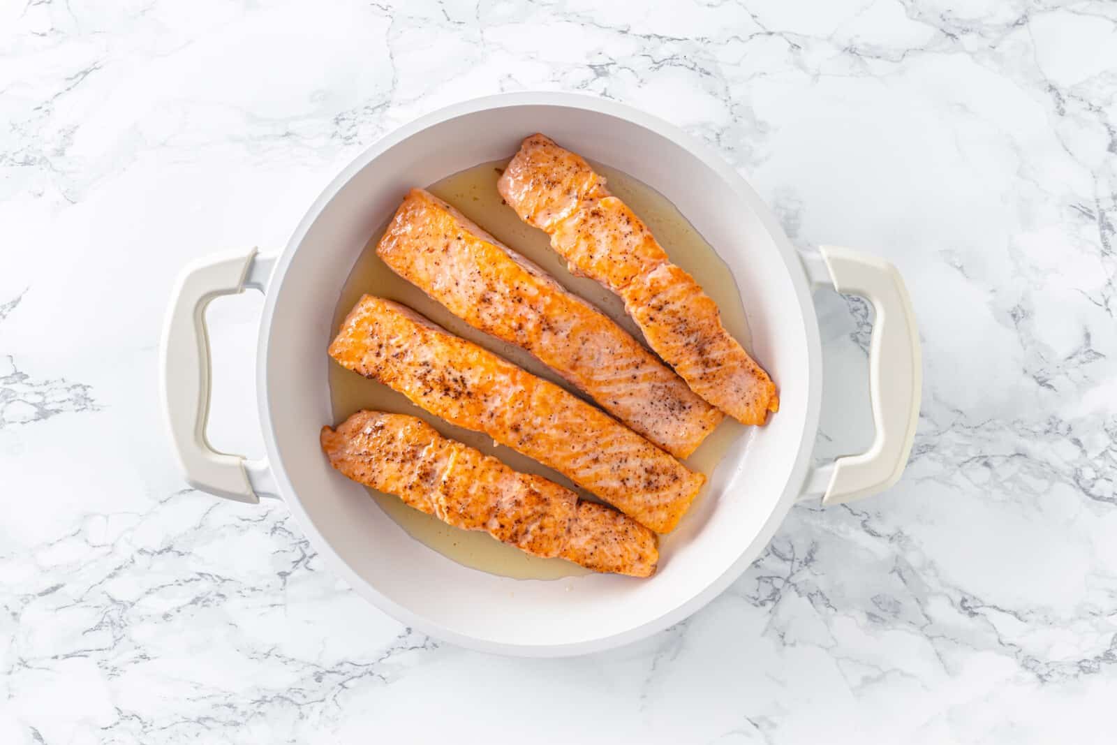 seasoned four salmon filets with salt and pepper in a pan.