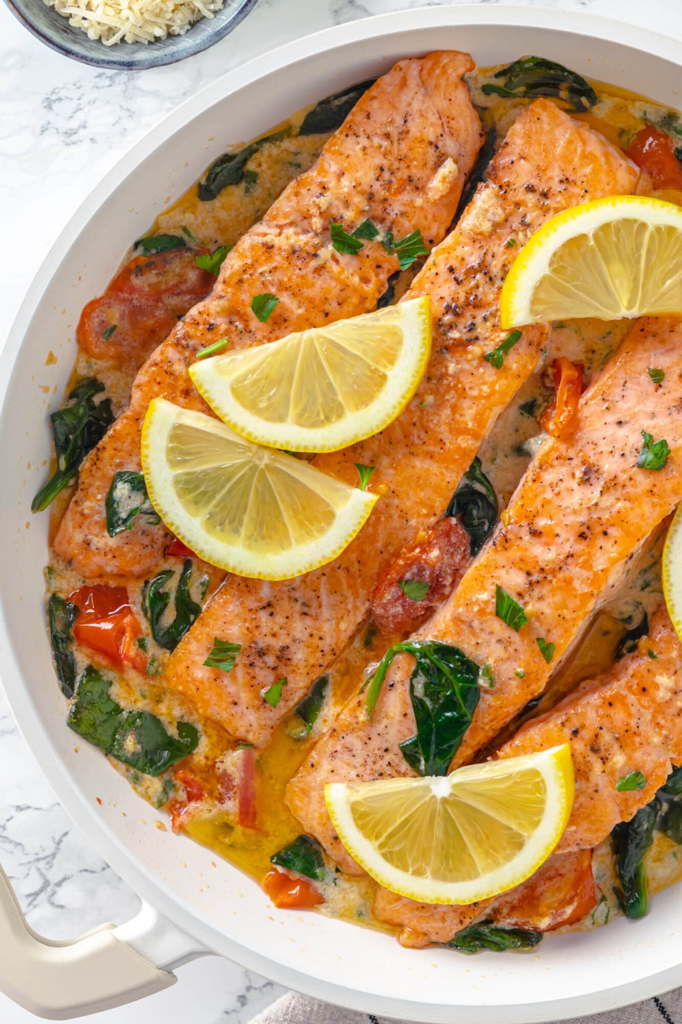 cooked salmon filets in a creamy butter sauce with tomatoes and spinach in a pan.